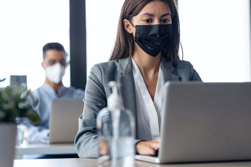 business partners wearing a hygienic face mask while working with laptops in the coworking space.