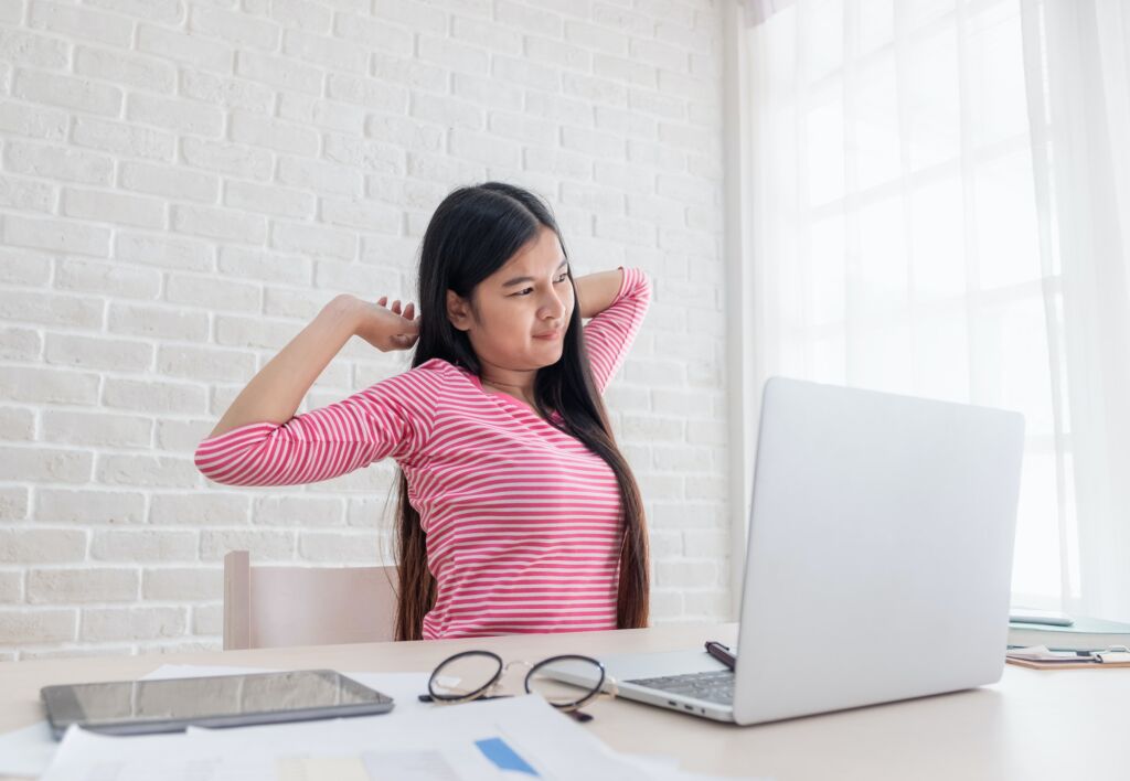 Asian woman freelancer stretching arm at back in front of laptop from work in home office